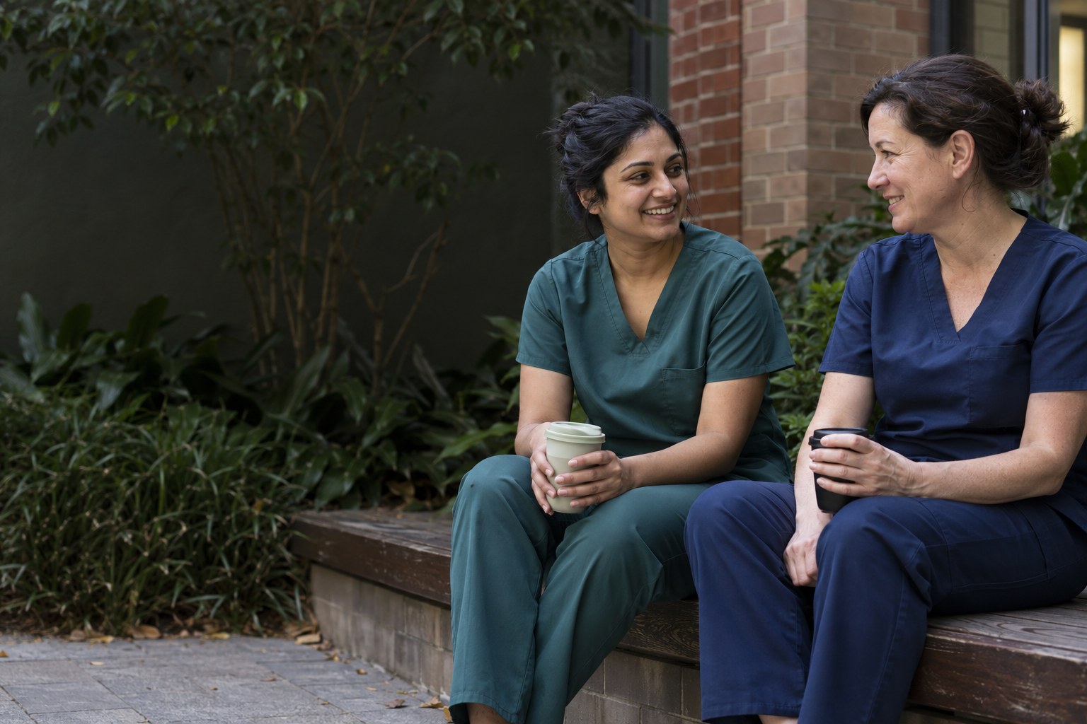 AI-generated concept: two colleagues in teal and navy scrubs sharing a quiet courtyard break